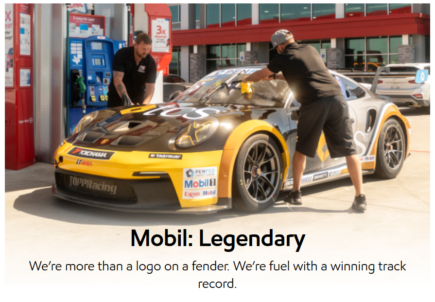 Two people clean the windshield of a black and yellow Porsche race car at a gas station.